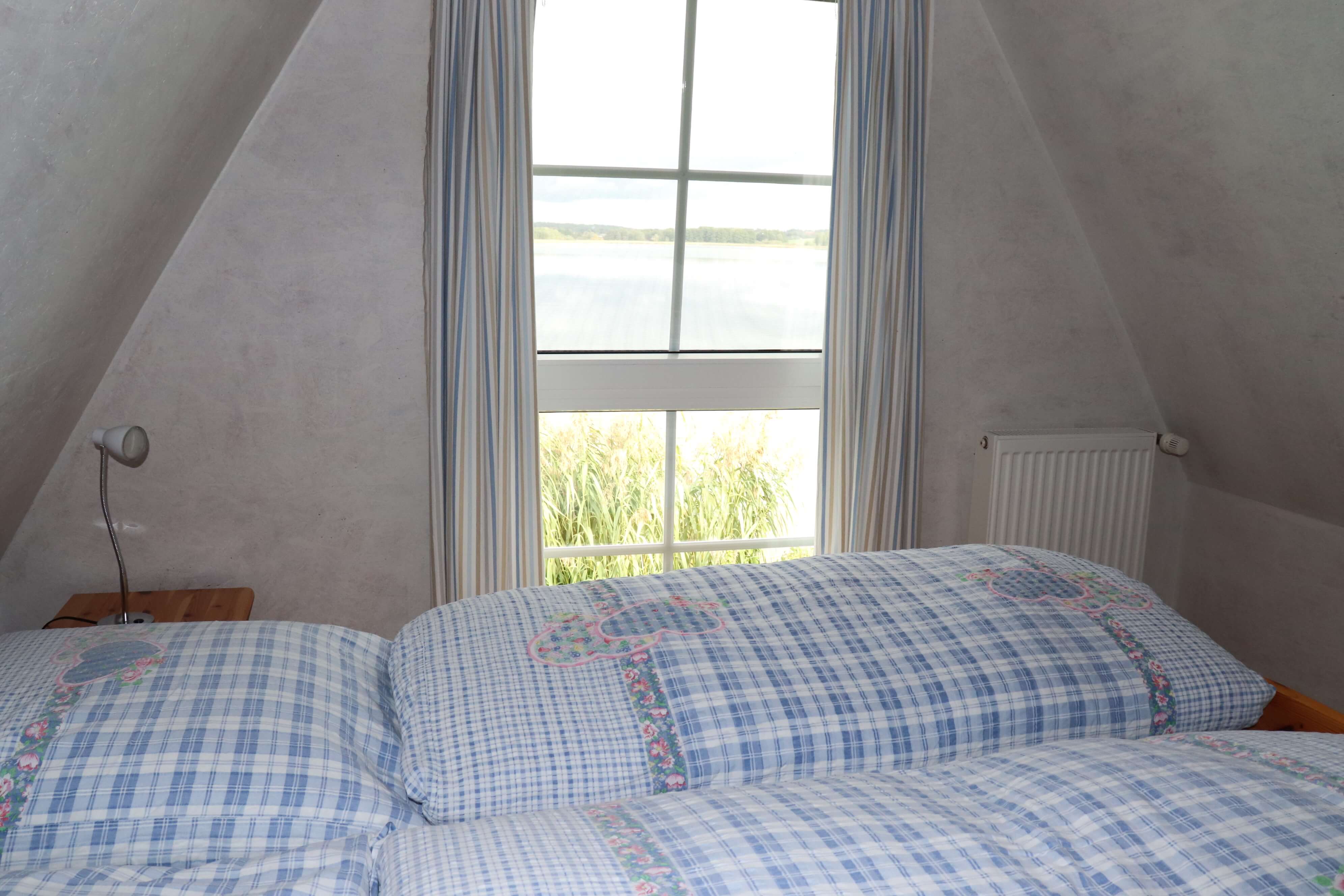 Schlafzimmer mit einem großen Doppelbett in Holzoptik und Ausblick auf den Sternberger See.
