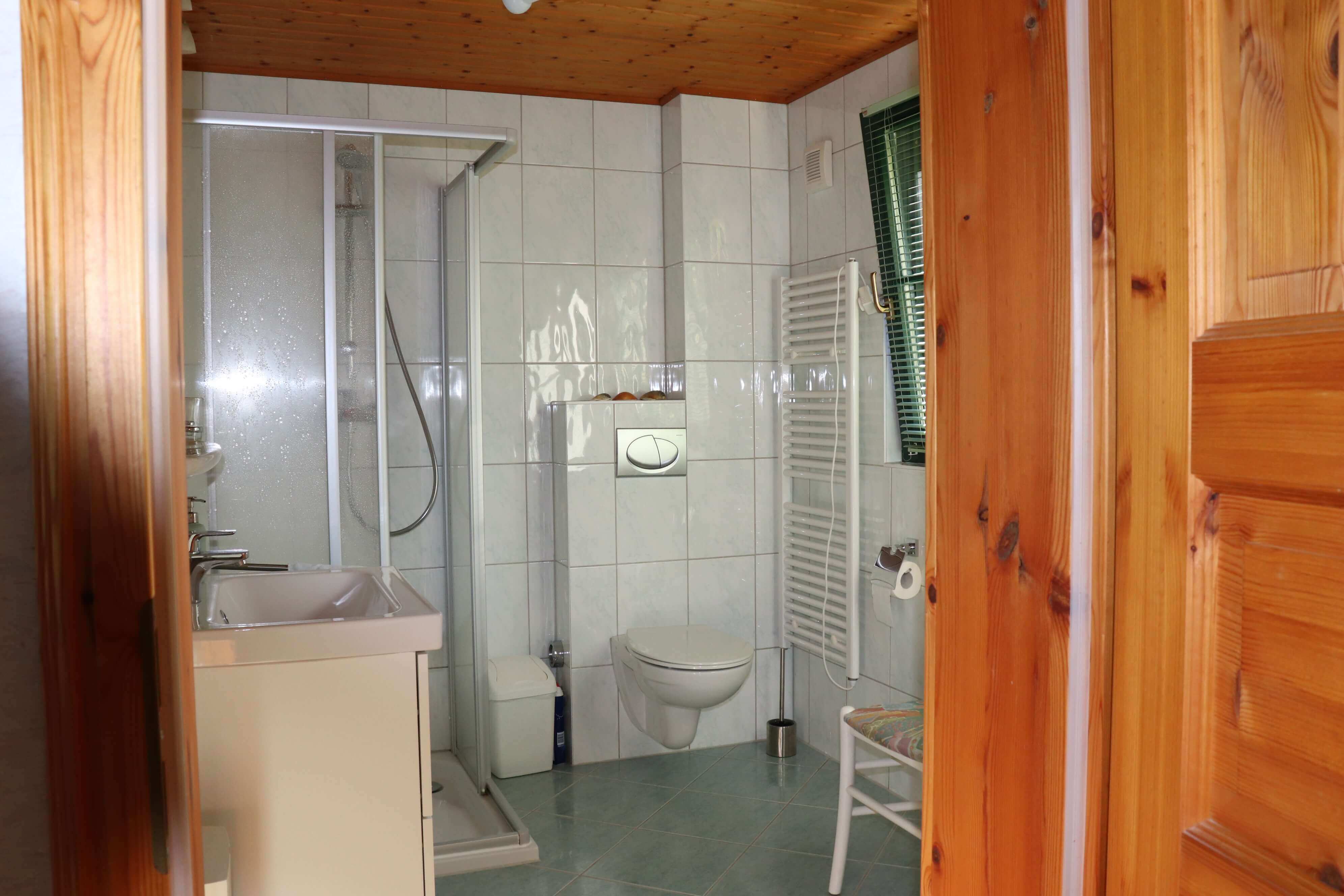 Weiß gefliestes Badezimmer mit einer Toilette, einer Dusche und einem Waschbecken.